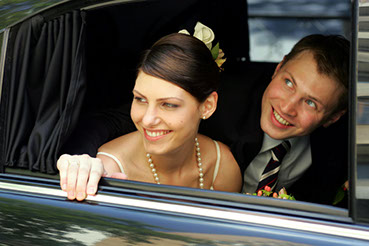 A couple celebrates their wedding day in Greenville, SC as their wedding party and guests cheer for them in their getaway limousine.